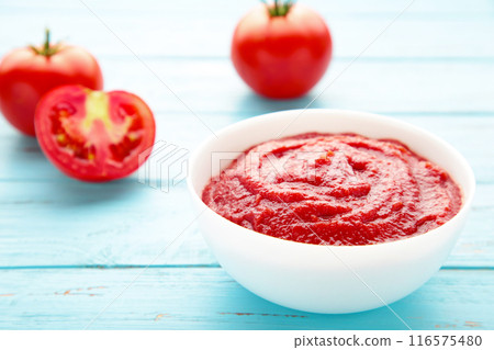 Tomato ketchup sauce in a bowl with tomatoes on blue wooden background. View from above. 116575480