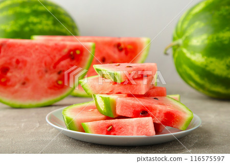 Fresh ripe striped sliced watermelon in the plate on grey background. Fresh ripe striped sliced watermelon in the plate on grey background. 116575597