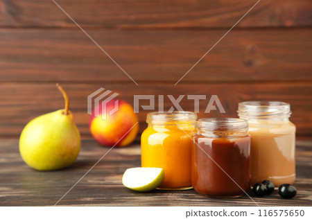 Glass jars with nutrient baby food and fruit on brown background Glass jars with nutrient baby food and fruit on brown background 116575650