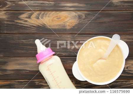 Milk and bowl with porridge for baby on brown background 116575690