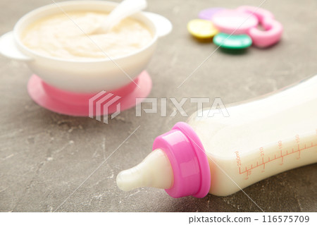 Milk and bowl with porridge for baby on grey background Milk and bowl with porridge for baby on grey background 116575709