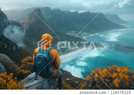 Man in orange jacket seated hilltop overlooking coastal mountains sea mist 116576324
