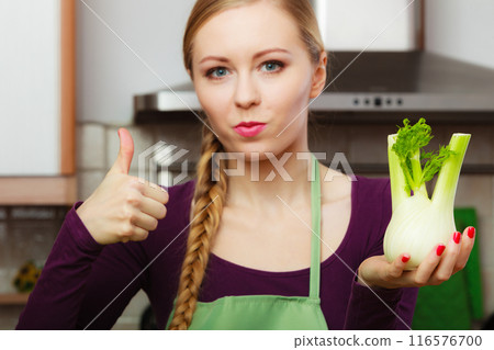 Woman in kitchen holds raw fennel bulb vegetable 116576700