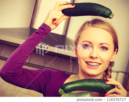 Woman in kitchen holds zucchini vegetable Woman in kitchen holds zucchini vegetable 116576727