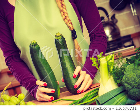 Woman in kitchen holds zucchini vegetable Woman in kitchen holds zucchini vegetable 116576731