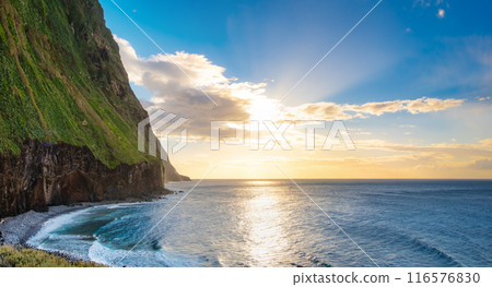 Volcanic rock cliffs Achadas da Cruz in backlit sunlight. Waves of the Atlantic Ocean. Beautiful sunset seascape of the resort island of Madeira, Portugal 116576830