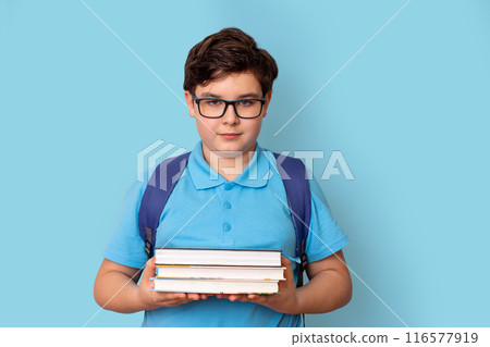 A cute schoolboy with backpack, in glasses and a blue T-shirt, holding a stack of books A cute schoolboy with backpack, in glasses and a blue T-shirt, holding a stack of books 116577919