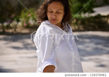 Woman in white shirt enjoying sunlight outdoors and looking down Woman in white shirt enjoying sunlight outdoors and looking down 116578461