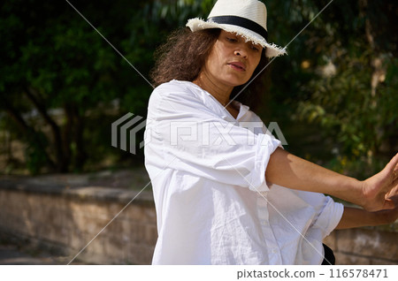 Woman in white shirt and hat stretching outdoors on a sunny day Woman in white shirt and hat stretching outdoors on a sunny day 116578471