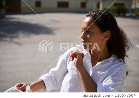 Thoughtful woman in white shirt standing outdoors in morning light 116578504