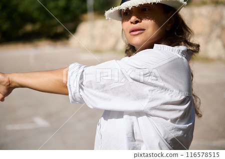 Woman in white shirt and hat confidently pointing forward in a sunny outdoor setting Woman in white shirt and hat confidently pointing forward in a sunny outdoor setting 116578515
