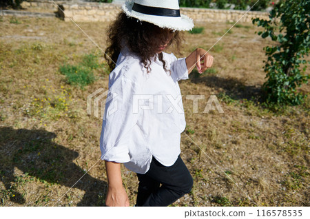 Woman in white shirt and straw hat walking outdoors on a sunny day 116578535