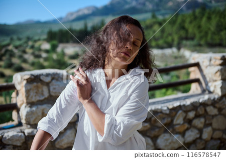 Woman in white shirt meditating outdoors with mountains and greenery in the background Woman in white shirt meditating outdoors with mountains and greenery in the background 116578547