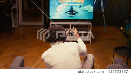 BIPOC gamer receiving winner screen on smart TV after killing all foes in science fiction game. Player celebrating after being victorious in SF videogame on console attached to television set 116578867