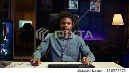 Professional gamer engaging in online competitive multiplayer match using cutting edge gaming setup. BIPOC man at home captivating spectators during live broadcast, playing videogames 116578872
