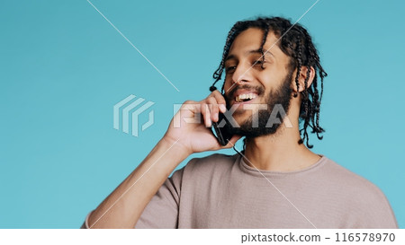 BIPOC man discussing with best friend over telephone call using smartphone. Cheerful person talking with mate in phone call using cellphone, isolated over studio background, camera B close up 116578970