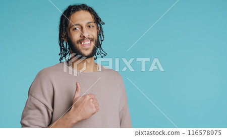 Man doing thumbs up hand gesturing, showing approval, having positive mood. Cheerful BIPOC person presenting confirmation, doing agreement finger sign, studio background, camera B Man doing thumbs up hand gesturing, showing approval, having positive mood. Cheerful BIPOC person presenting confirmation, doing agreement finger sign, studio background, camera B 116578975