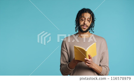 Middle Eastern man reading book from publisher aloud, telling story, enjoying hobby. BIPOC person narrating literature novel, doing critique essay, isolated over studio background, camera A 116578979