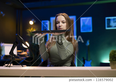 Young entertainer presenting laptop from brand sponsoring video, urging viewers to purchase it. Girl does influencer marketing by advertising digital device to audience in studio 116579002