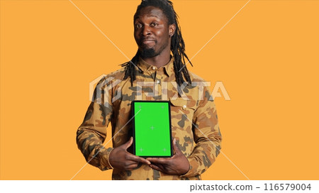 African american adult with greenscreen on gadget, presenting isolated chromakey display and smiling in front of camera. Young adult holding mobile device with copyspace blank layout. 116579004