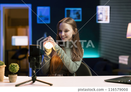 Cheerful young influencer filming review of light bulb able to change into different colors. Tech enthusiast showcasing smart home automation technology controlled by voice comwomands Cheerful young influencer filming review of light bulb able to change into different colors. Tech enthusiast showcasing smart home automation technology controlled by voice comwomands 116579008