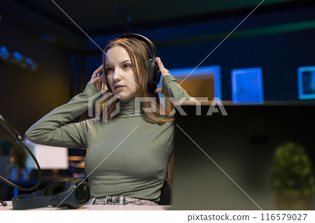 Gen Z online show host listening music through headphones before offering them during giveaway for loyal viewers. Teenage girl entertainer hosting online contest for fans with audio tech as prize Gen Z online show host listening music through headphones before offering them during giveaway for loyal viewers. Teenage girl entertainer hosting online contest for fans with audio tech as prize 116579027