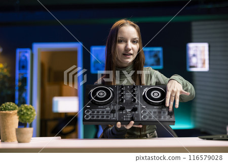 Portrait of girl mixing on DJ turntables, doing music production tutorial for internet streaming channel. Gen Z content creator playing around with stereo sound mixer in studio Portrait of girl mixing on DJ turntables, doing music production tutorial for internet streaming channel. Gen Z content creator playing around with stereo sound mixer in studio 116579028