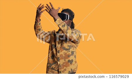Cool person using virtual reality headset on camera, enjoying 3d vision and interactive metaverse simulation on vr glasses. Modern adult having fun with goggles, artificial intelligence concept. Cool person using virtual reality headset on camera, enjoying 3d vision and interactive metaverse simulation on vr glasses. Modern adult having fun with goggles, artificial intelligence concept. 116579029