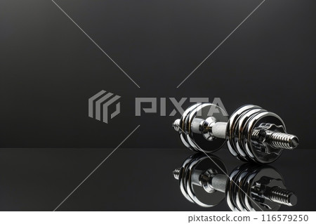 Metallic dumbbells resting on a reflective surface with copy space Metallic dumbbells resting on a reflective surface with copy space 116579250