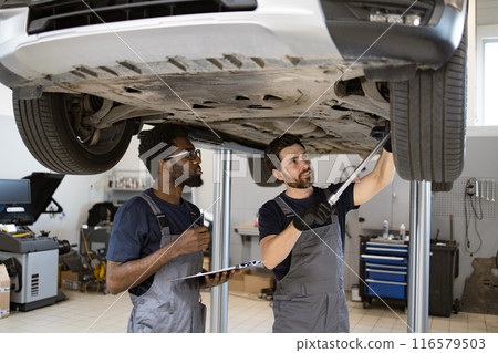 Two mechanics checking vehicle chassis on hydraulic lift 116579503