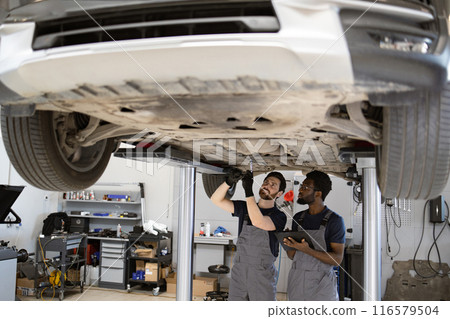 Two mechanics inspecting car undercarriage in auto repair shop 116579504