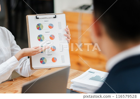 Colleagues discussing financial data and charts during a business meeting. Focus on clipboard with colorful graphs. 116579528