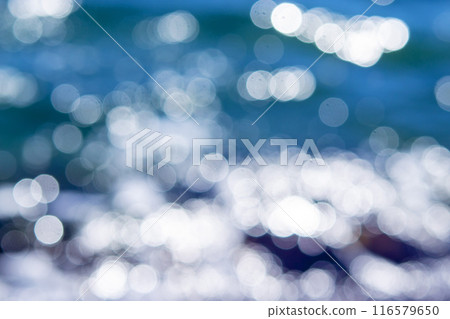 Sea waves rolling and crashing on the rocks with lots of white bokeh spots of sun glare on the surface of the ripples on the water. Sea view on a sunny summer day. Blurred abstract natural background 116579650