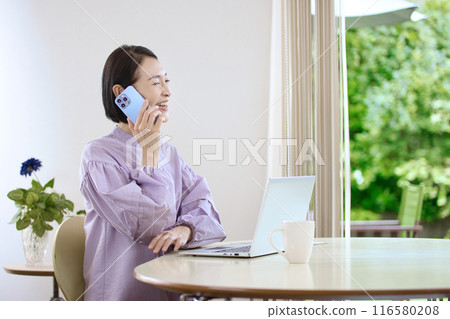 中年婦女在客廳一邊看電腦一邊操作智慧型手機 116580208