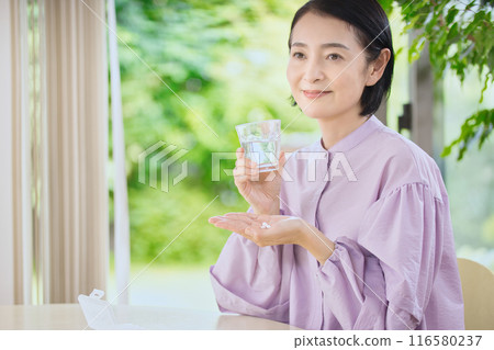 Smiling middle-aged woman taking medicine in the living room 116580237