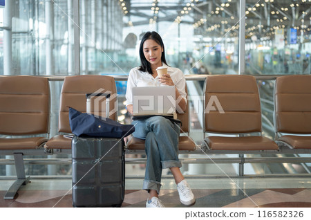 A beautiful Asian businesswoman sits at a waiting seat in the airport and working on her laptop. A beautiful Asian businesswoman sits at a waiting seat in the airport and working on her laptop. 116582326