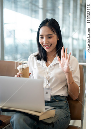 A businesswoman sits at a waiting seat in the airport, having an online meeting before boarding. A businesswoman sits at a waiting seat in the airport, having an online meeting before boarding. 116582328