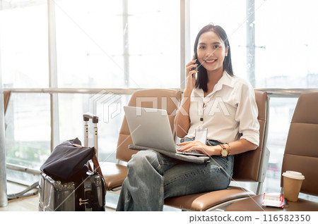 A confident Asian businesswoman is talking on the phone and working on her laptop in the airport. 116582350