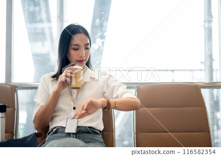 A confident Asian female passenger is having coffee and checking the time on her wristwatch. A confident Asian female passenger is having coffee and checking the time on her wristwatch. 116582354