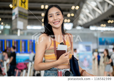 An attractive Asian female tourist with her belongings and passport is standing in the airport. An attractive Asian female tourist with her belongings and passport is standing in the airport. 116582399