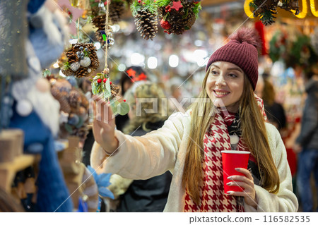 Young woman in souvenir shop examines Christmas handmade toys 116582535