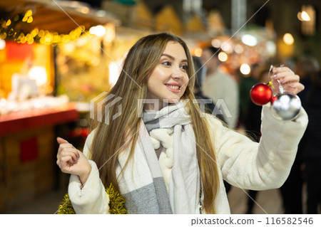 Woman at New Year fair and bustle is leisurely examining ball for decorating Christmas tree. 116582546
