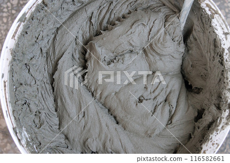 A bowl of grayish brown substance is being stirred with a spoon. The mixture appears to be a type of 116582661