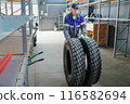 A man is holding two tires in a warehouse. The tires are black and are on a shelf 116582694