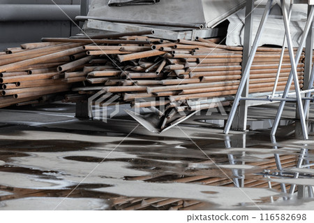 A pile of metal pipes is on the ground. The pile is large and has a lot of pieces. The image has a 116582698