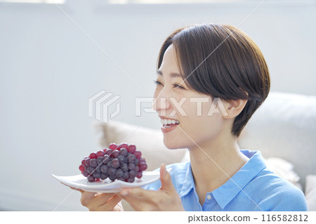 Woman eating grapes at home, looking at camera Woman eating grapes at home, looking at camera 116582812