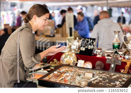 Happy female tourist looking to buy glass ashtray at flea market 116583652