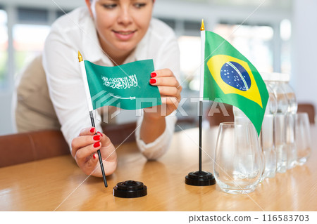 Little flag of Brazil on table and flag of Saudi Arabia put next to it by young woman 116583703