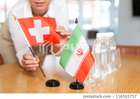 Little flag of Iran on table and flag of Switzerland put next to it by young woman 116583757