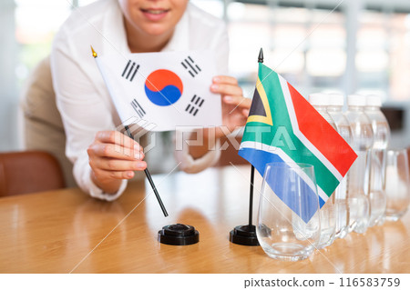Little flag of South Africa on table and flag of South Korea put next to it by young woman Little flag of South Africa on table and flag of South Korea put next to it by young woman 116583759